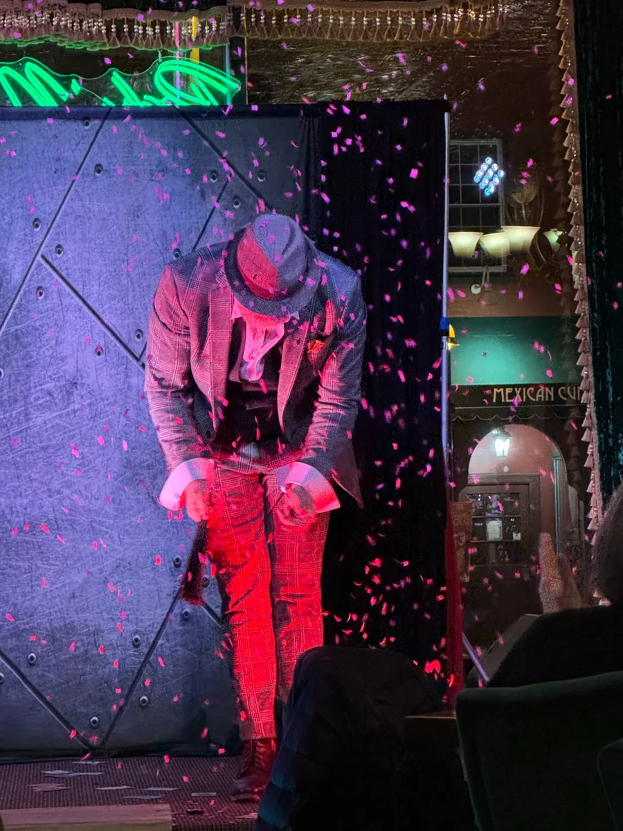 Mike DiDomenico taking a bow on the Club Arcada stage with pink confetti falling in dramatic red and blue lighting