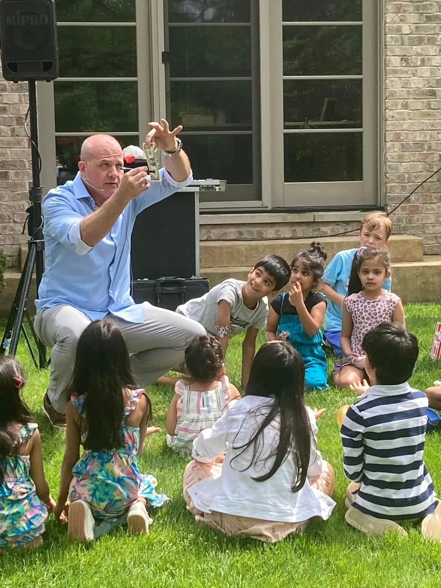 Group of children watching Mike DiDomenico perform magic at an outdoor backyard birthday party