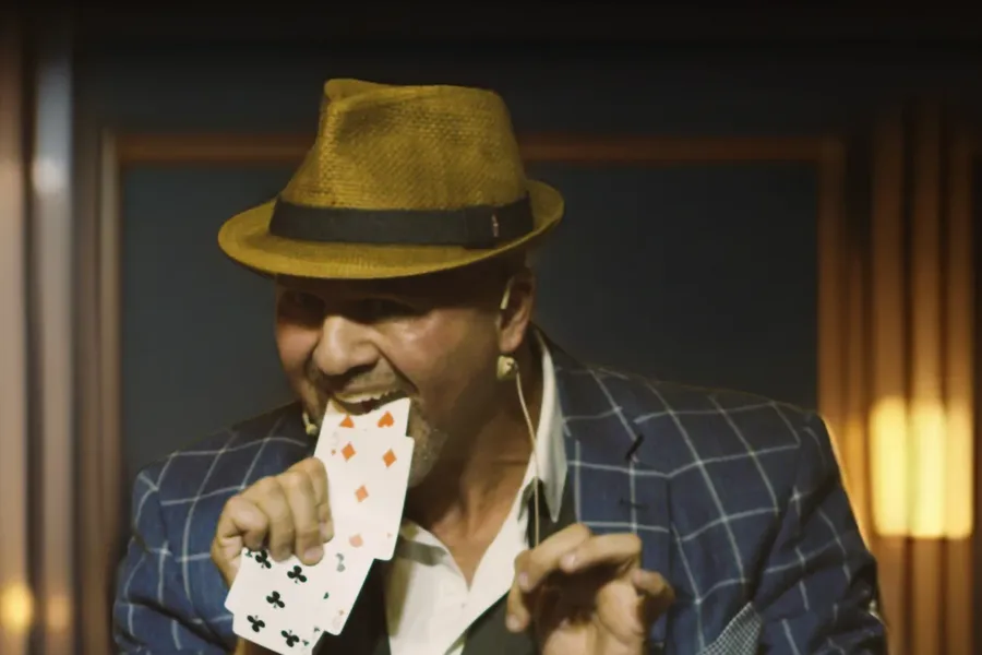 Mike DiDomenico in plaid suit and fedora with playing cards in his mouth during performance at Club Arcada