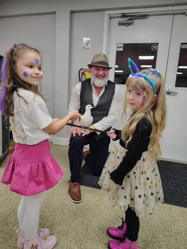 Two girls with face paint holding white dove on magic wand at community event
