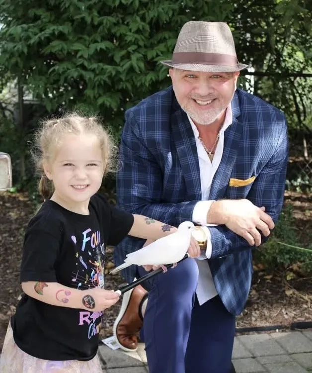 Mike DiDomenico kneeling with little girl holding white dove at outdoor birthday party