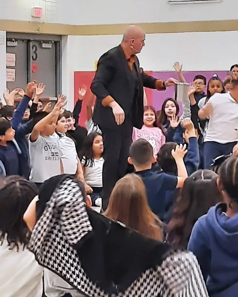 Children with hands raised in excitement during Mike DiDomenico school assembly