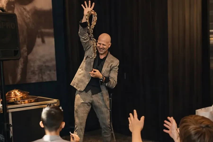 Mike DiDomenico holding python above his head on stage as well-dressed audience members raise their hands in excitement at luxury private event