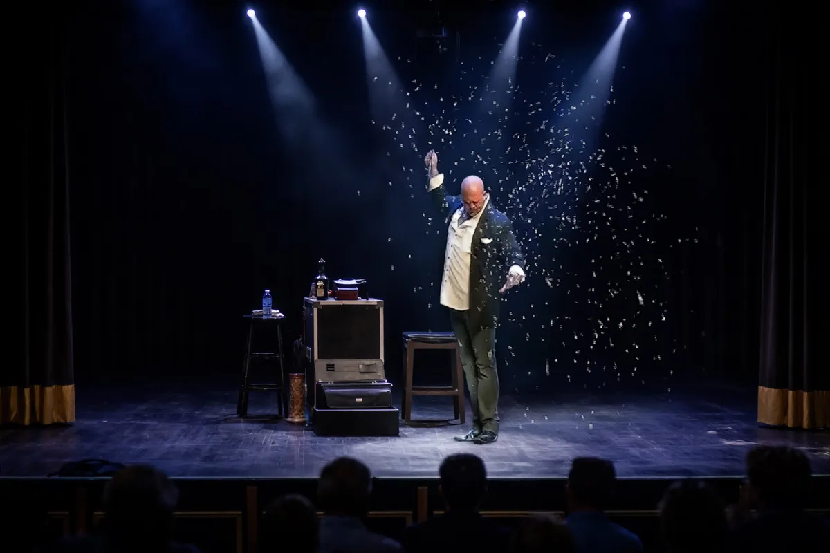 Mike DiDomenico performing on a professional theater stage with dramatic lighting and snow confetti falling around him