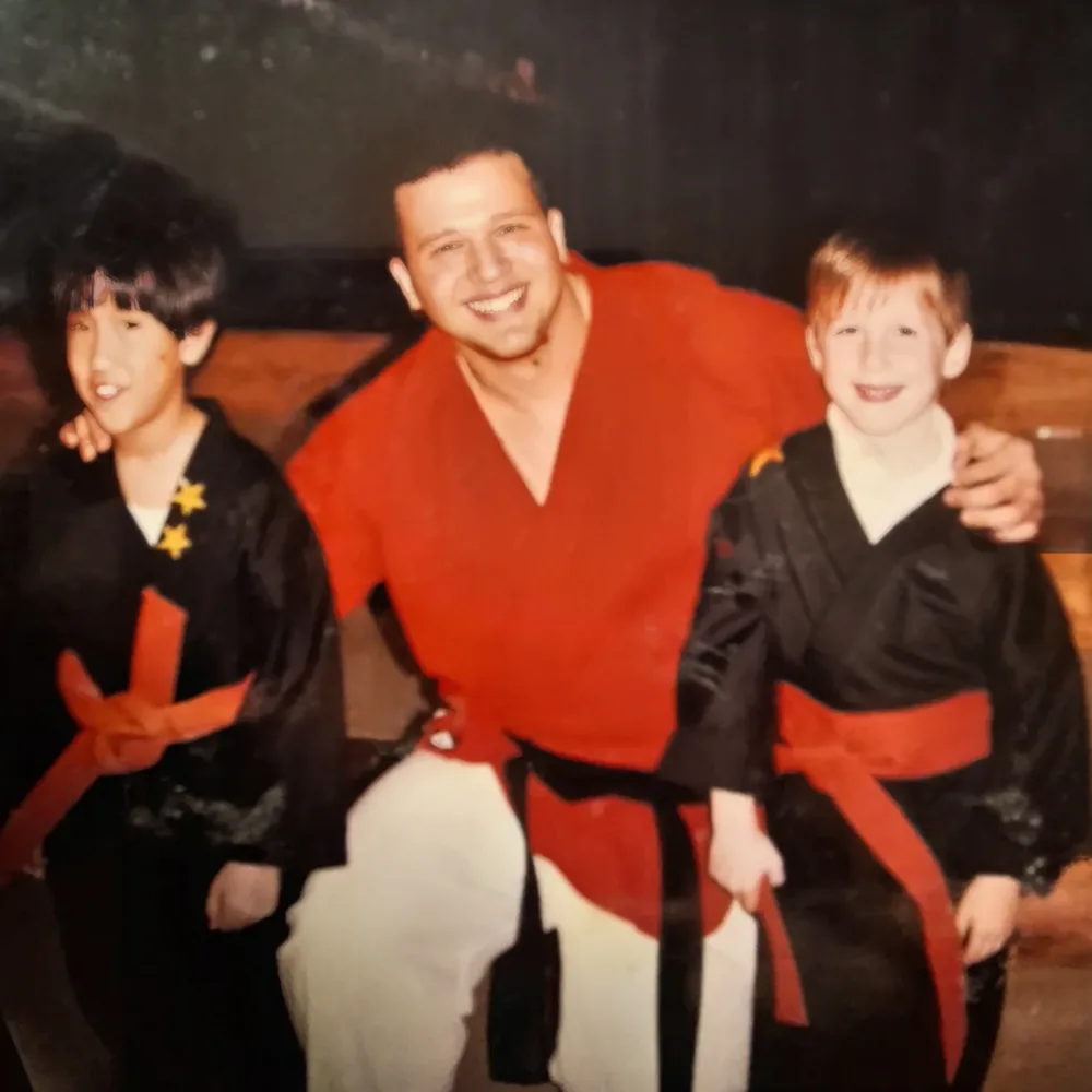 Young Mike DiDomenico in red gi teaching martial arts to two young students at Champion Youth Outreach